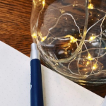 jar with string lights beside a plain notebook and pen